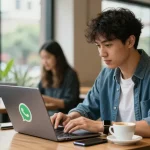 Person using laptop to download WhatsApp下載 in a lively café setting with modern equipment.
